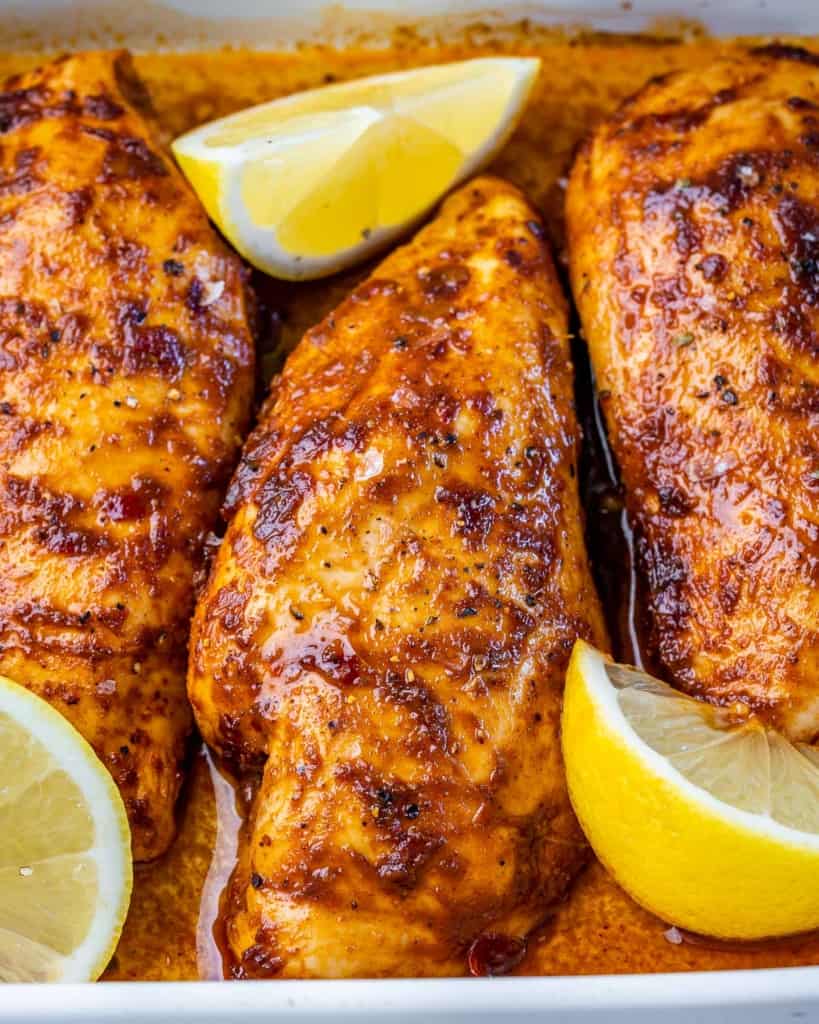 close up image of a baked chicken breast in a dish with lemon garnishes