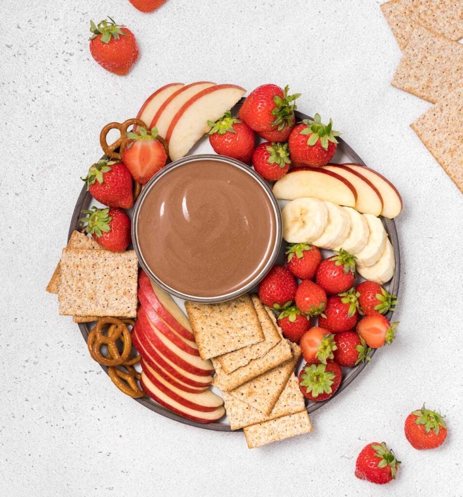 top view of chocolate fruit dip over a plate with fruits and crackers 