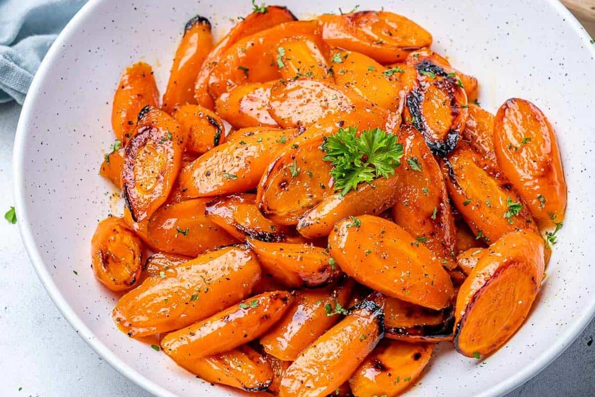 glazed carrots coated with honey, roasted and placed in a white bowl.