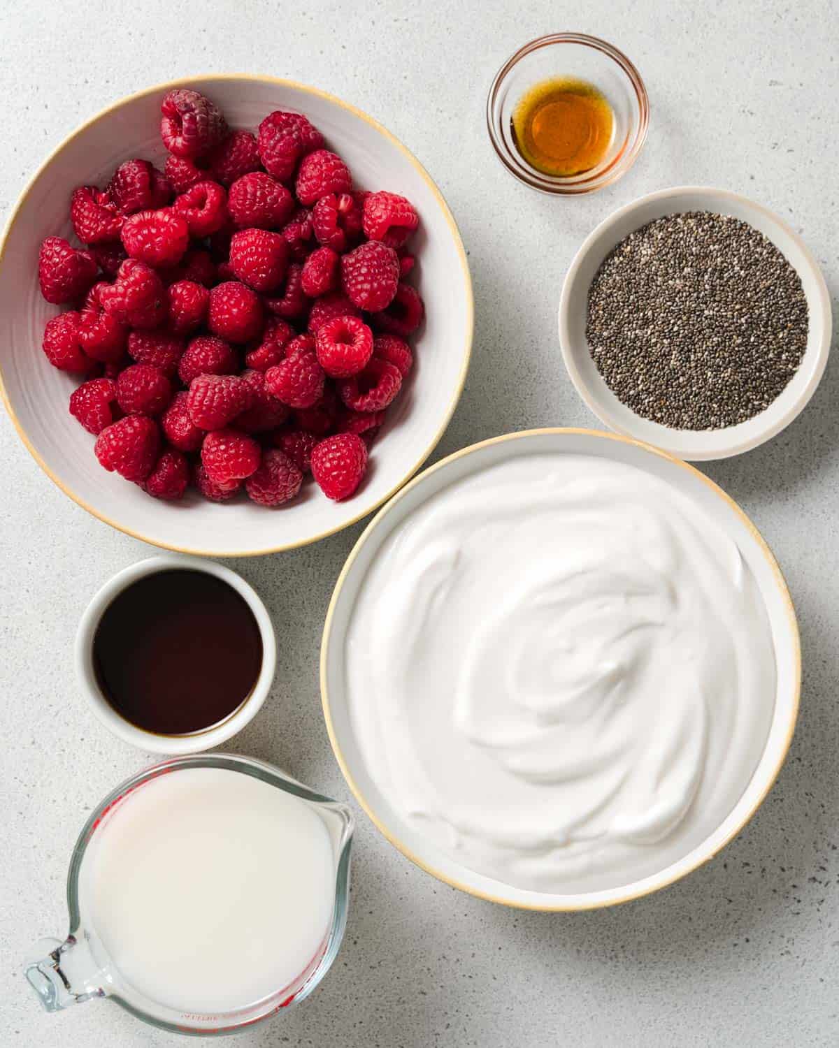 Raspberries, yogurt, chia seeds, milk, and maple syrup in small bowls.
