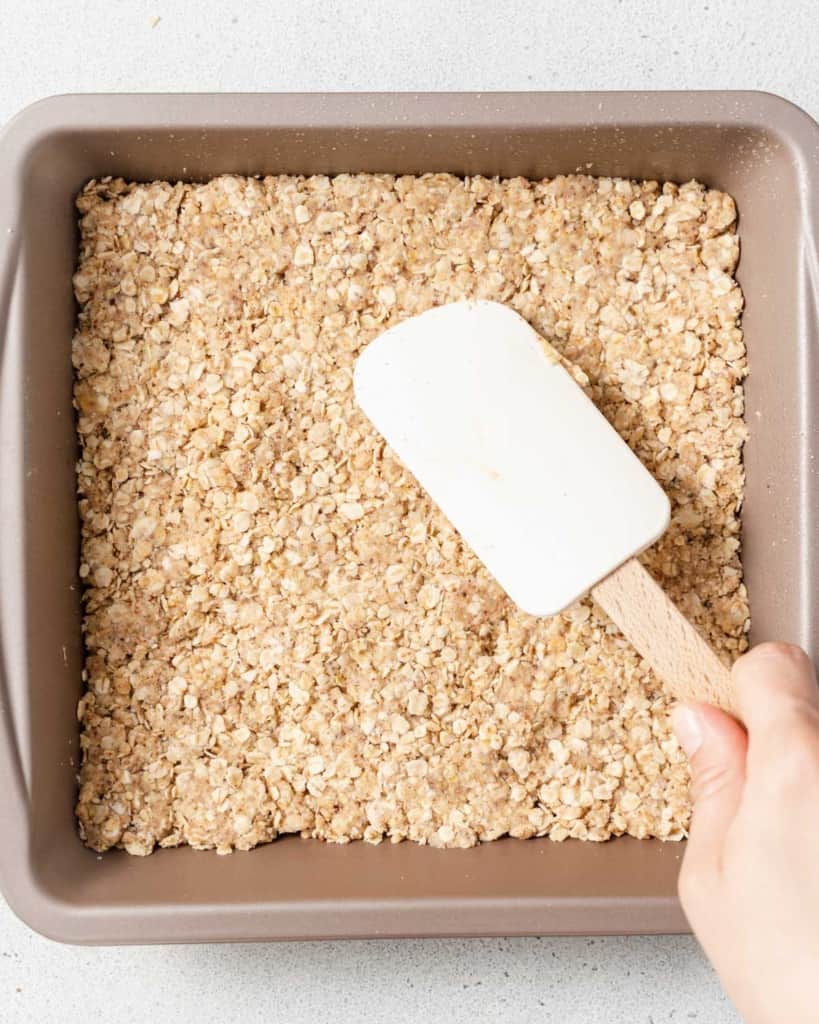 Using a spatula to spread oat crumbs.