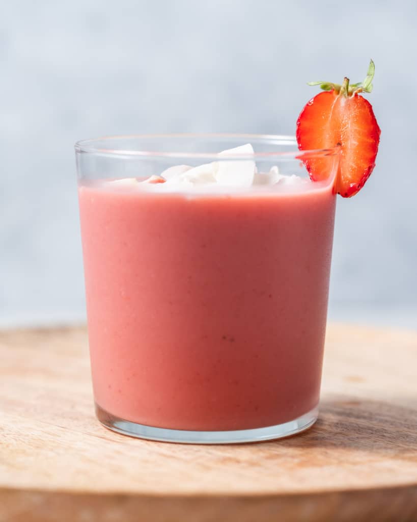 Smoothie in a glass garnished with coconut flakes and a fresh strawberry.