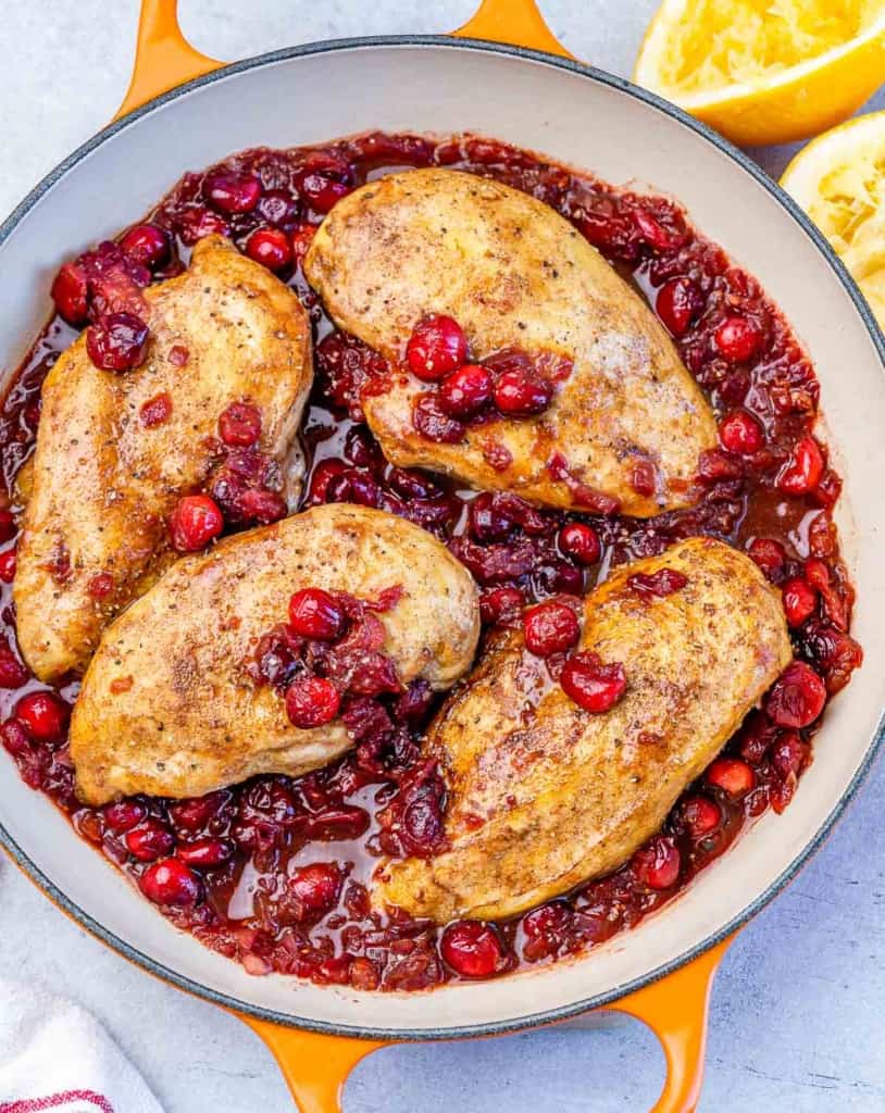 top view of 4 baked chicken breast over a bead of cranberry sauce in an orange skillet