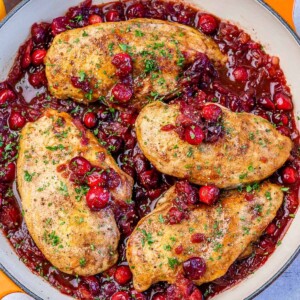 Top view of a skillet with 4 cooked chicken breast in a cranberry sauce.