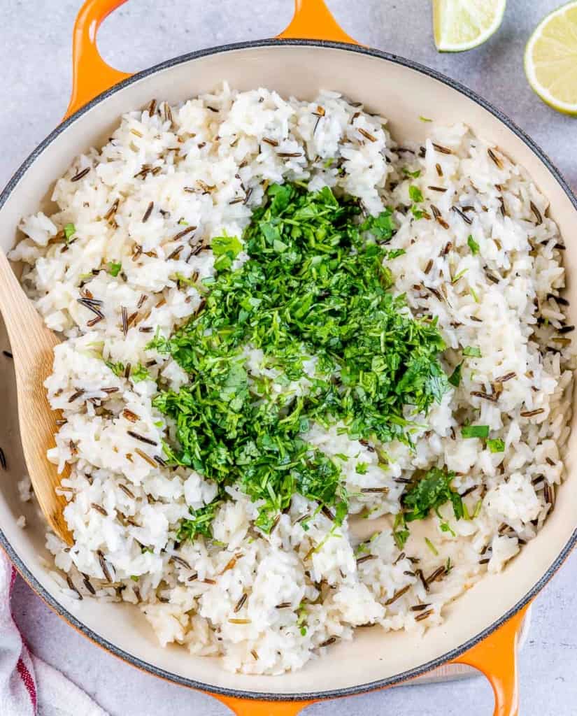 Adding cilantro to rice in a pan.