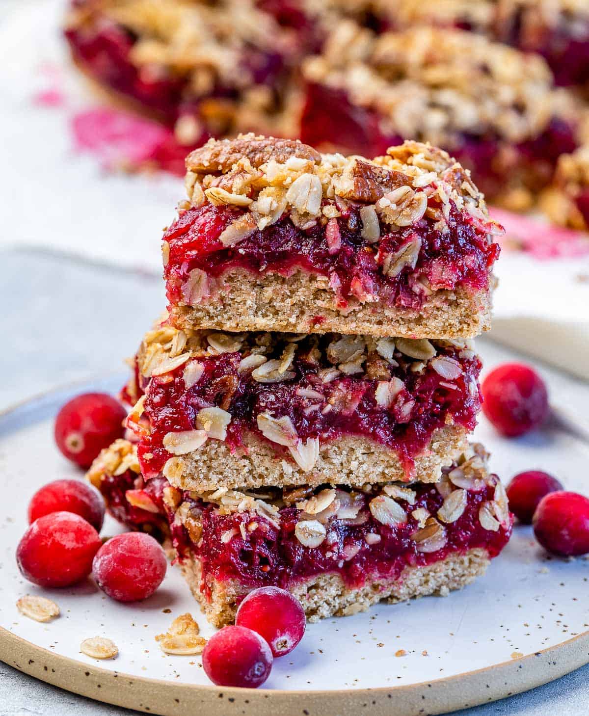 Cranberry oatmeal bars stacked on a plate with fresh cranberries on the side.