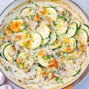 Top view of creamy sautéed zucchini with mushrooms on an orange skillet.