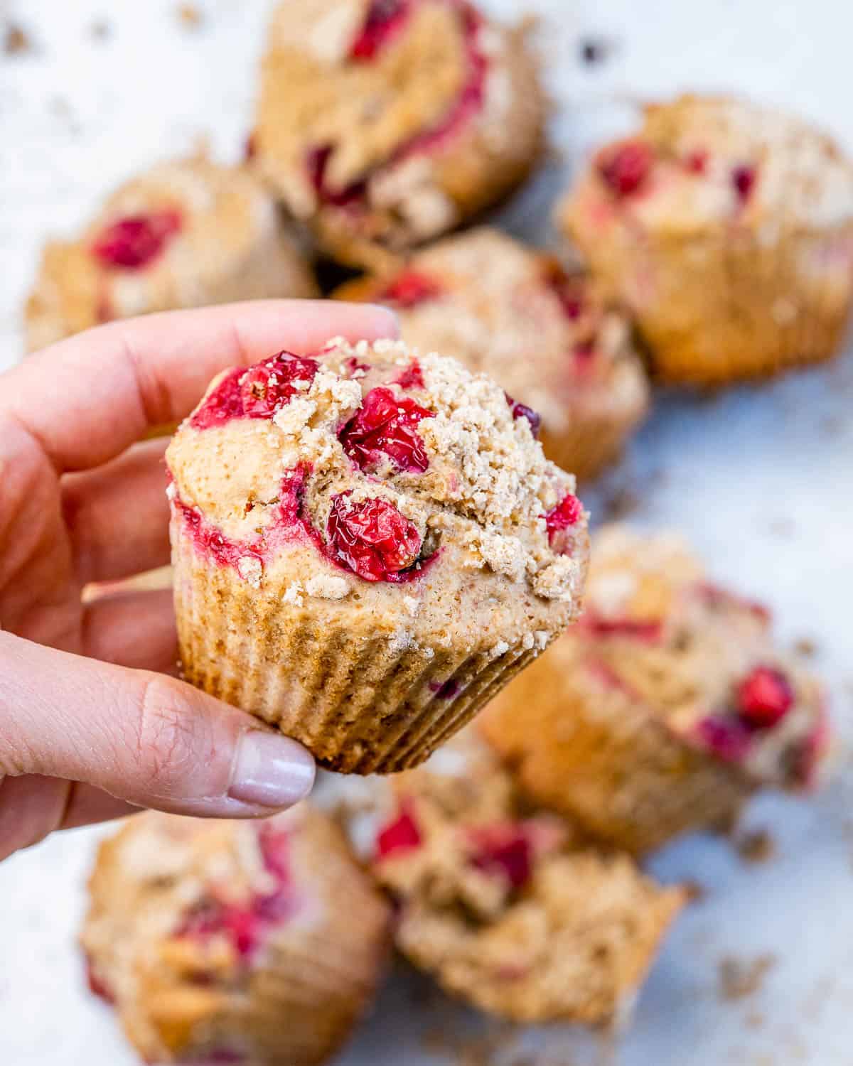Woman's hand holding a orange cranberry muffin.