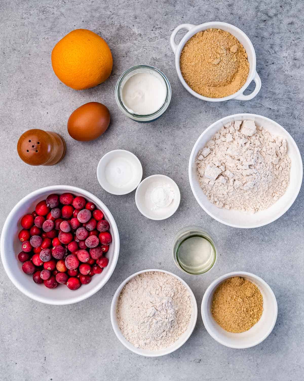 Flour, sugar, egg, yogurt and fresh cranberries divided into bowls.