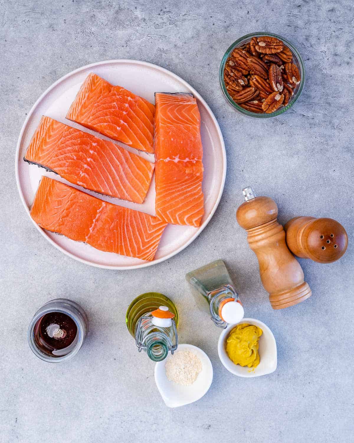 Raw salmon filets, pecans, olive oil, and seasonings divided into small portions.