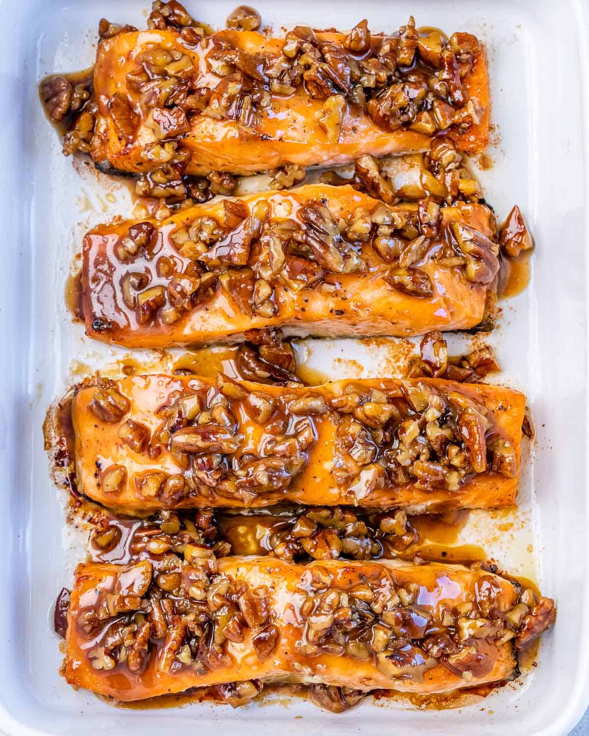 Top view of baked salmon topped with pecans glazed with maple syrup in a white baking dish.