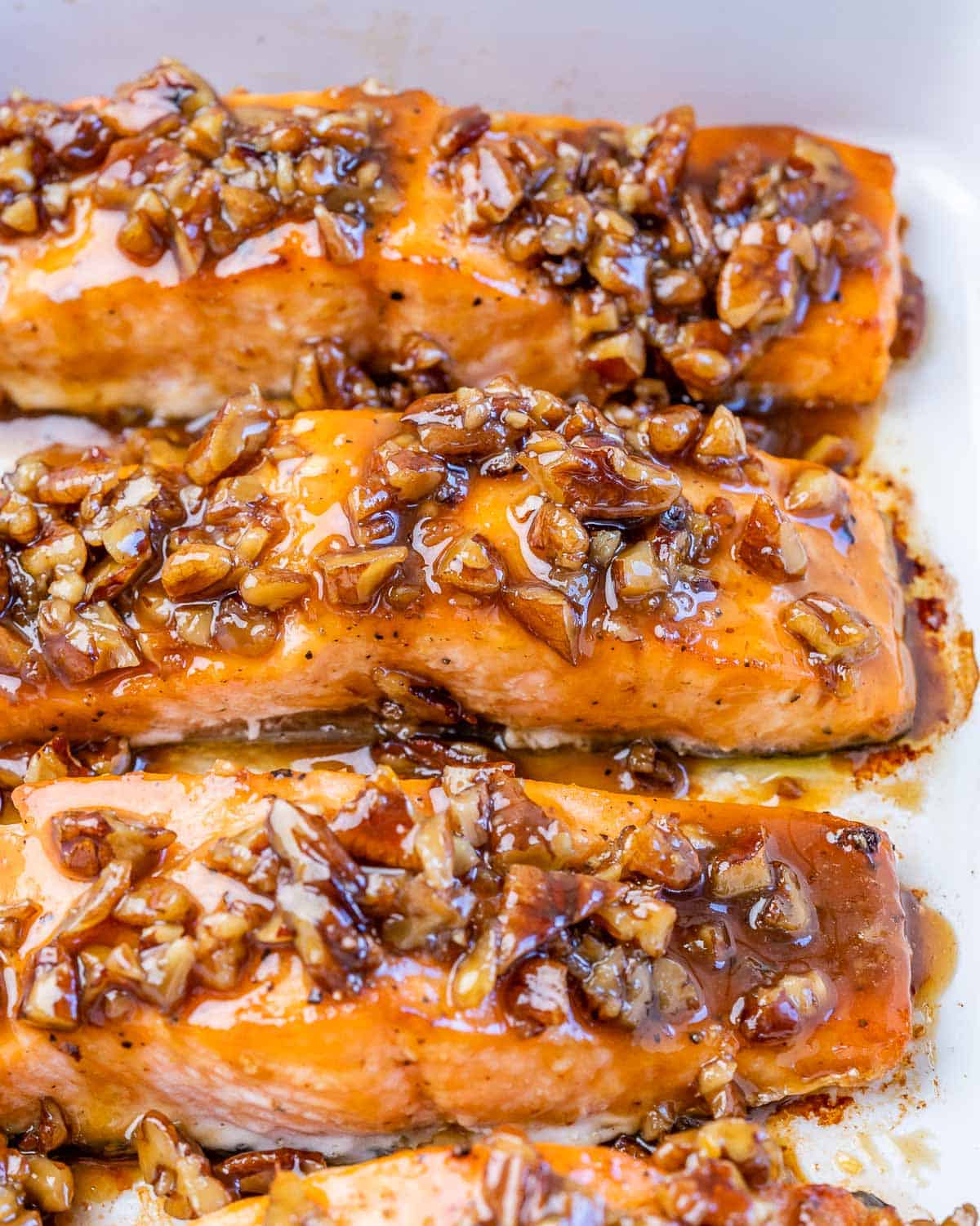 Filets of salmon topped with a maple pecan glaze in a white dish.