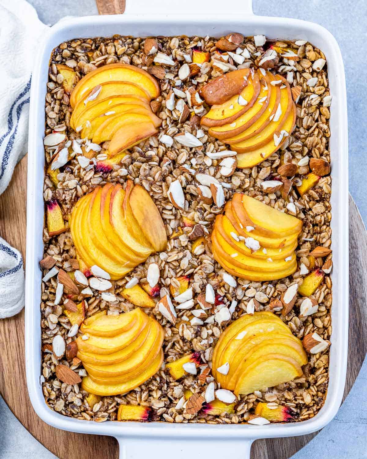 Top view of baked oatmeal in a white baking dish with slices of peach on top.