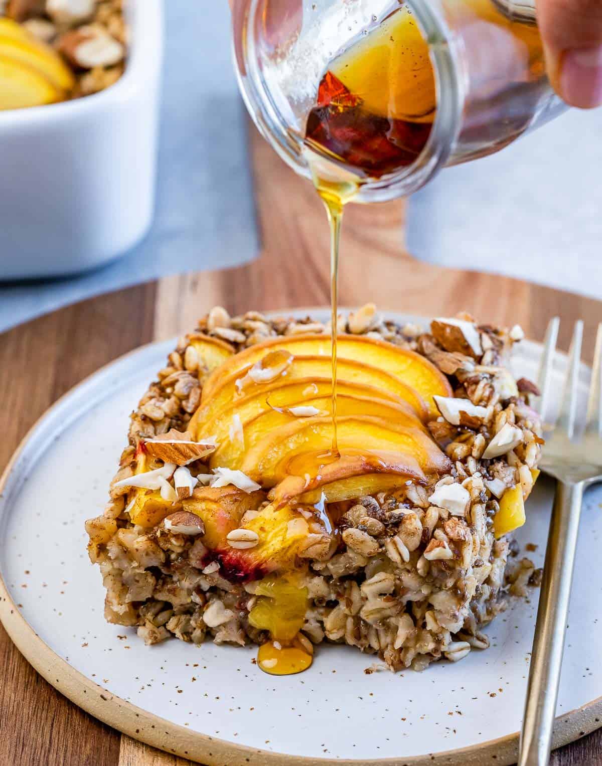 Drizzling maple syrup over a slice of peach oatmeal bake.