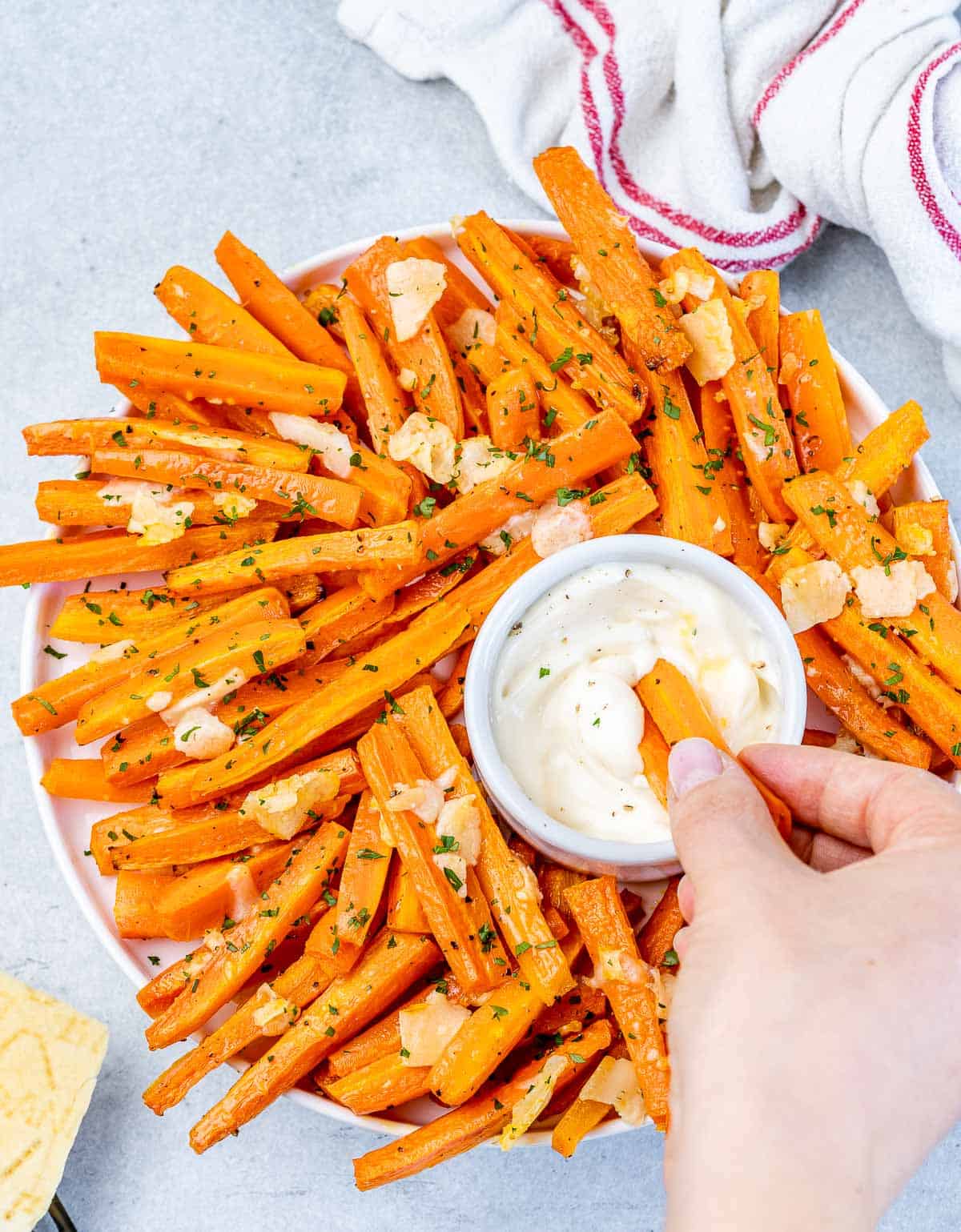 Hand dipping carrot fries into bowl of sauce.