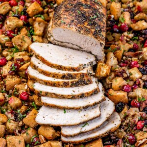 Side shot of sliced baked turkey breast over a bed of stuffing with cranberries.