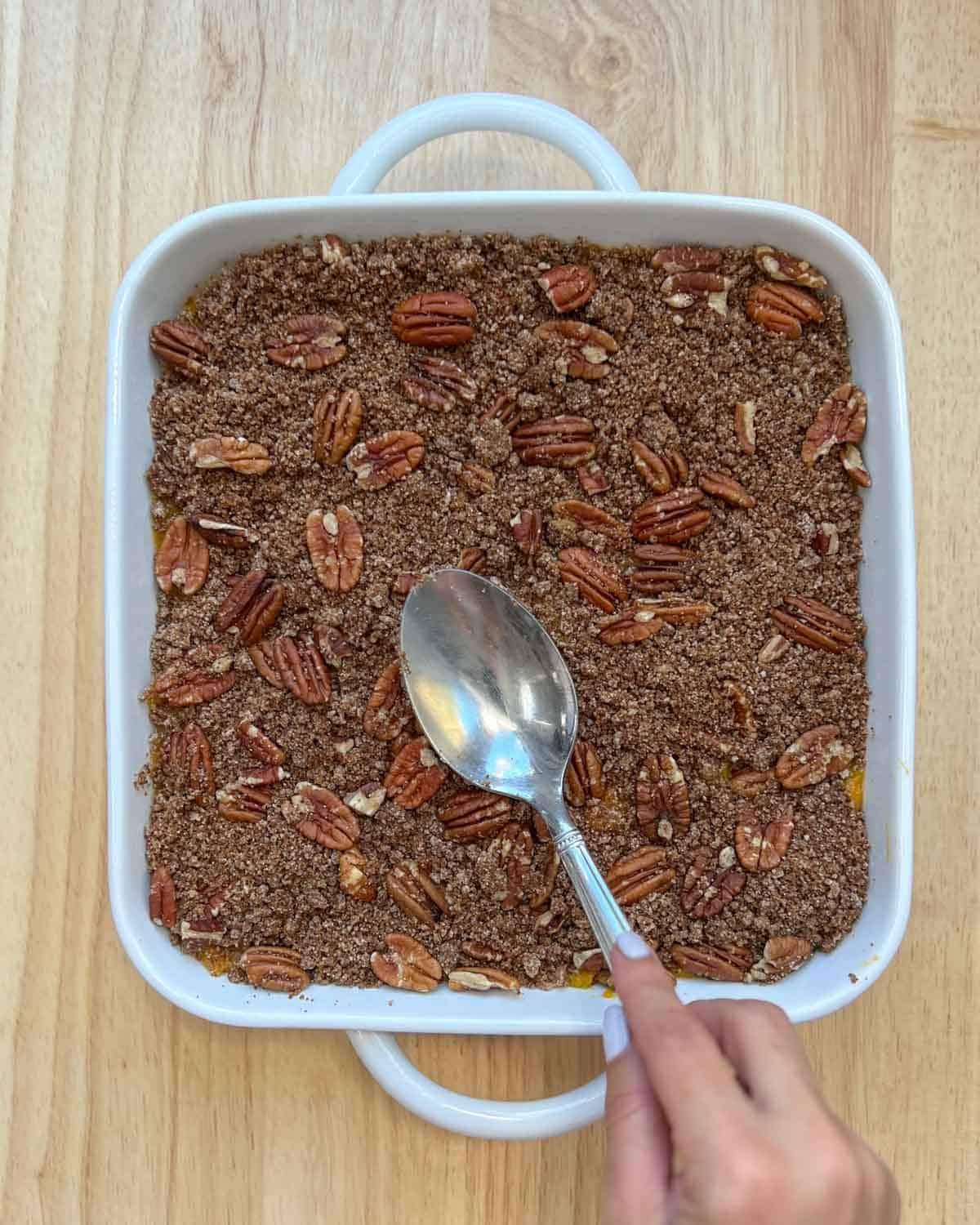 Pecan and flour topping are added over the squash base in a dish.