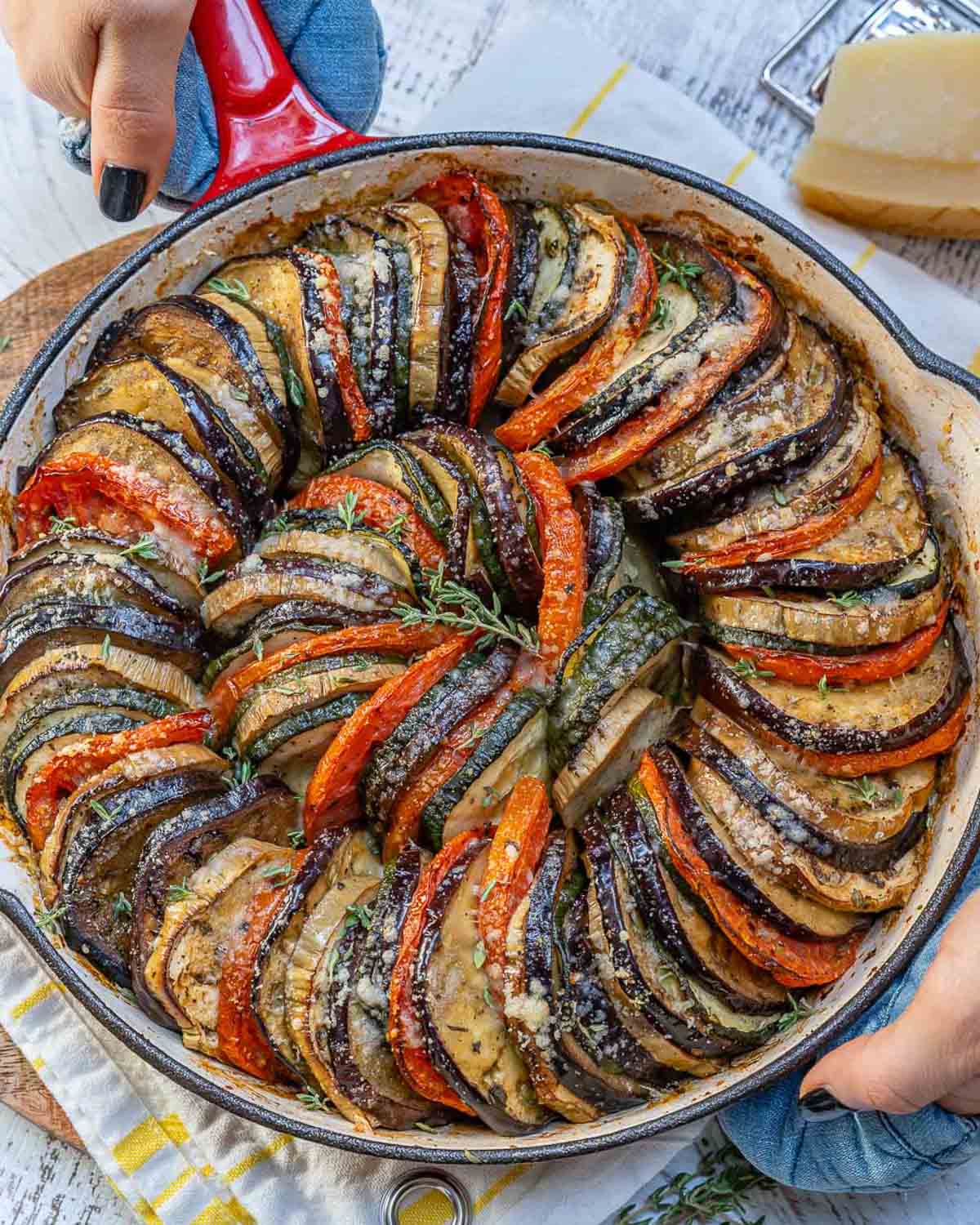 hand holding a skillet with eggplant and zucchini gratin.