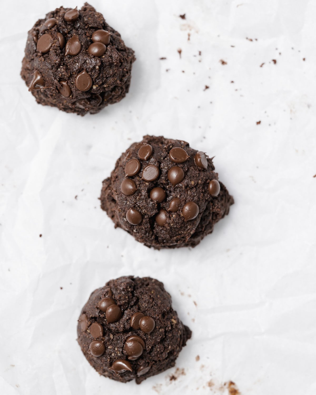 Top view of 3 chocolate brownie cookies on a white parchment paper.