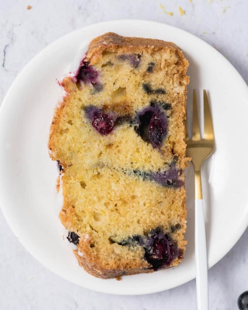 a slice of blueberry bread on a plate with a fork on the right of it
