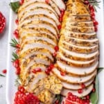 sliced roasted boneless turkey breast on a plate with pomegranate arils.
