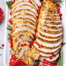 sliced roasted boneless turkey breast on a plate with pomegranate arils.