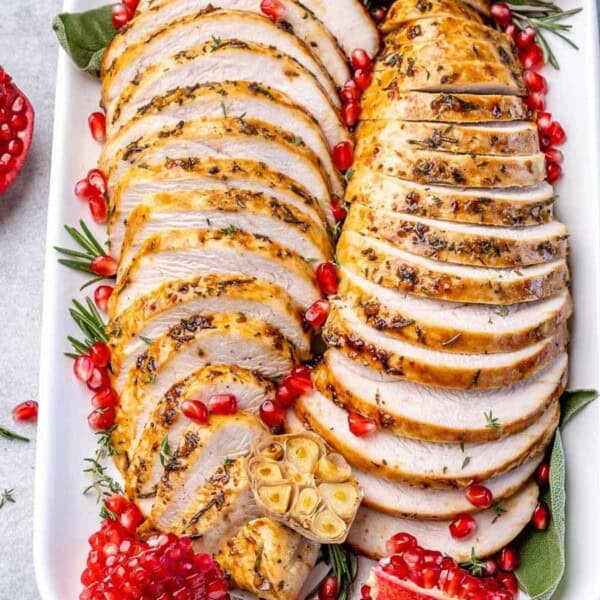 sliced roasted boneless turkey breast on a plate with pomegranate arils.