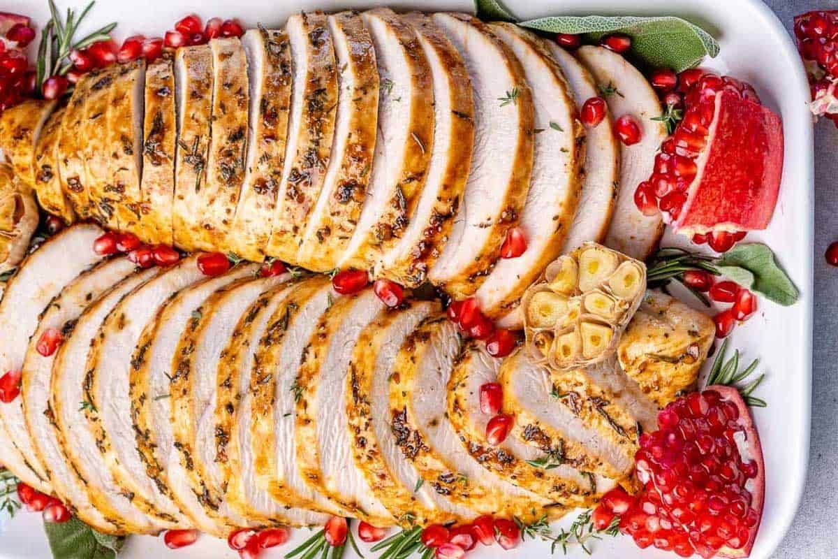sliced roasted turkey breast on a plate with pomegranate garnish.