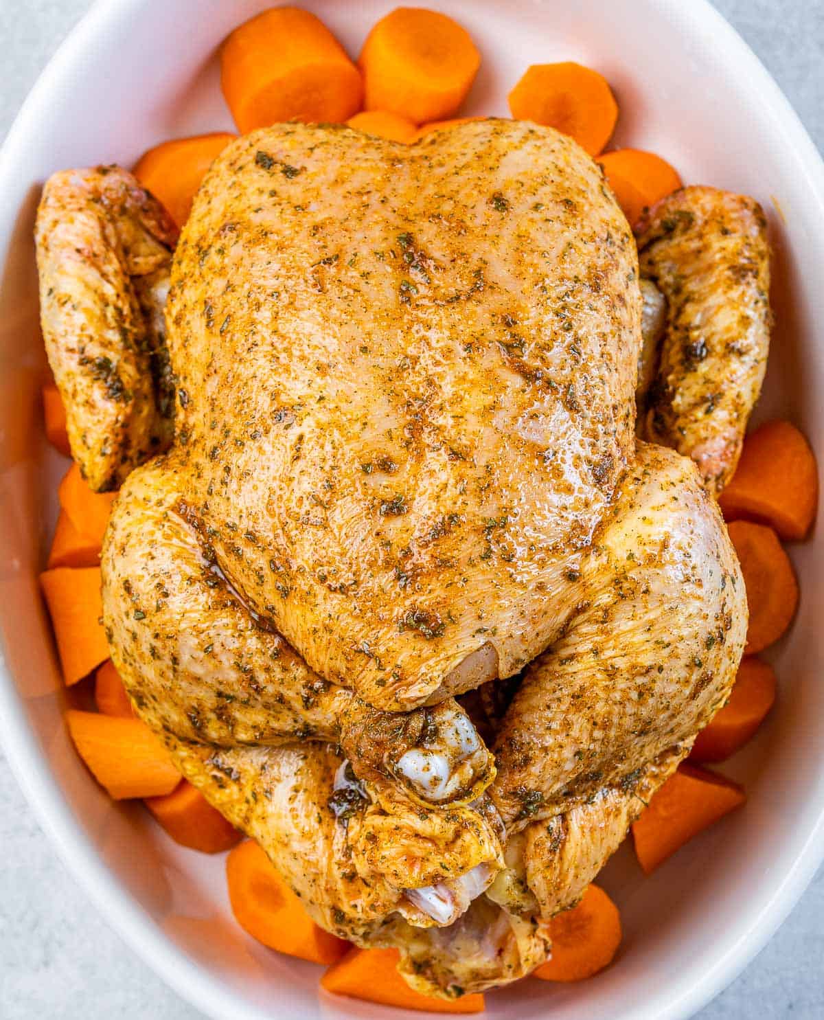 Seasoned chicken in a dish over chopped carrots.