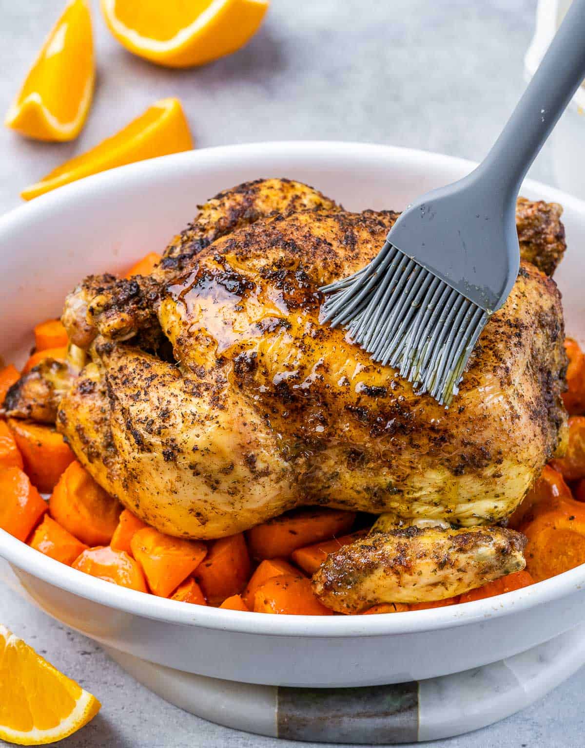 Basting whole chicken with maple glaze in a baking dish.