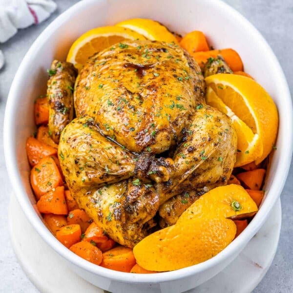 top view of a whole baked chicken over chopped carrots in a white dish