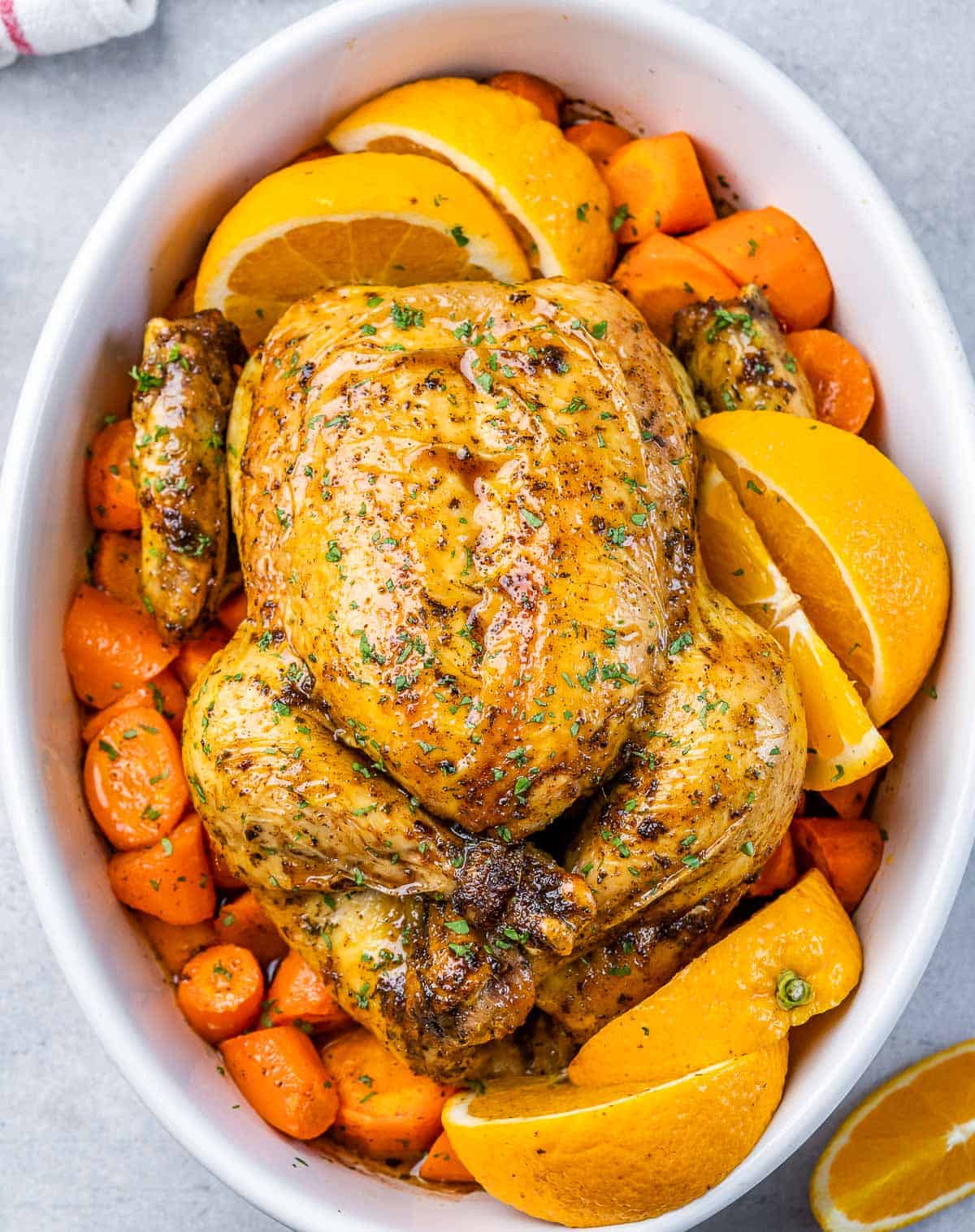 Top view of a whole baked chicken over chopped carrots in a white dish.