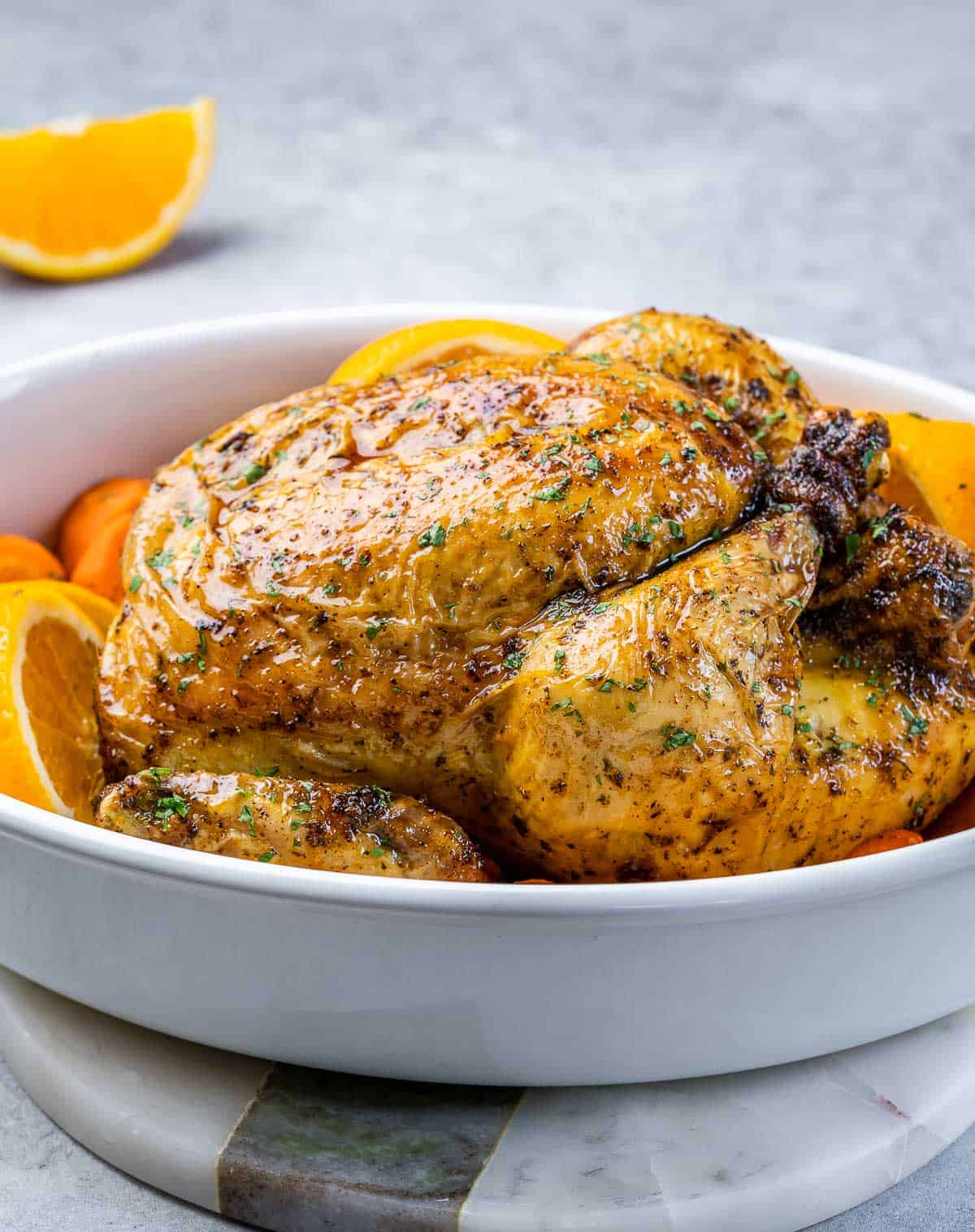 Baked whole chicken in a white casserole dish.