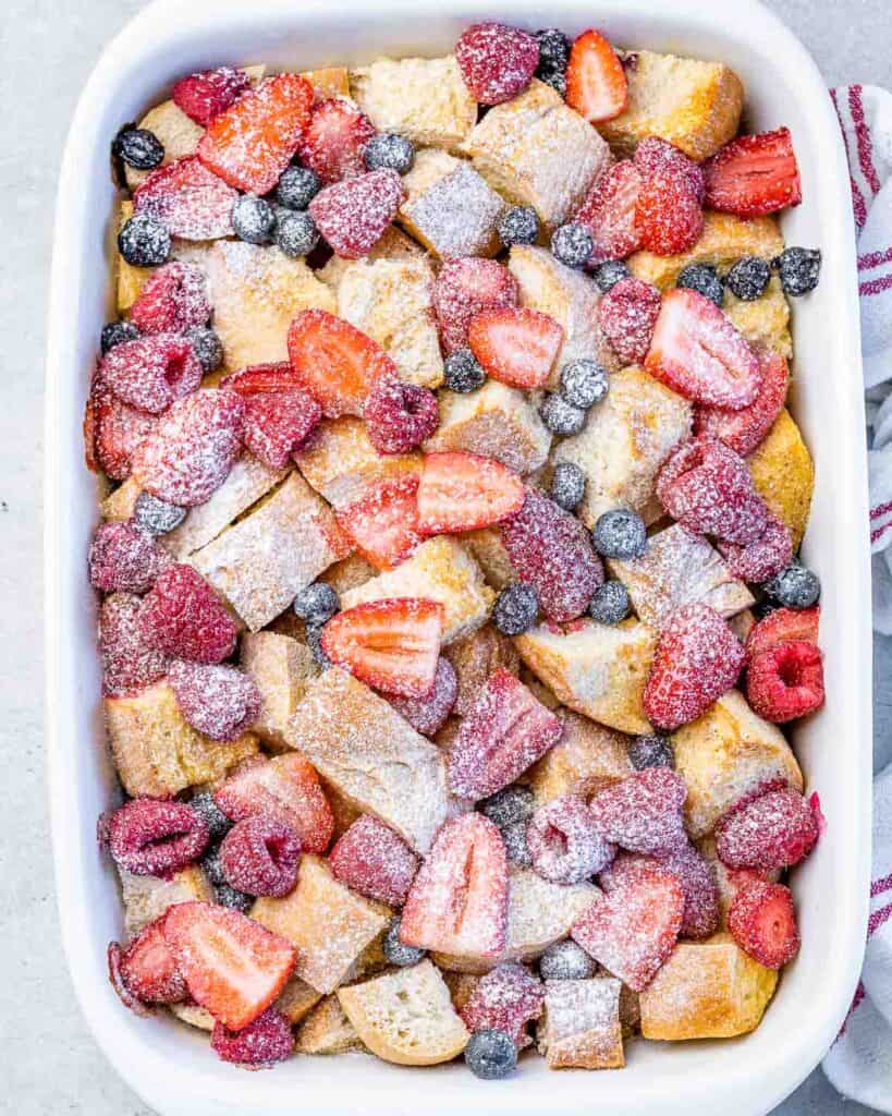 top view of a white dish with baked french toast topped with fresh cut berries and white powder sugar