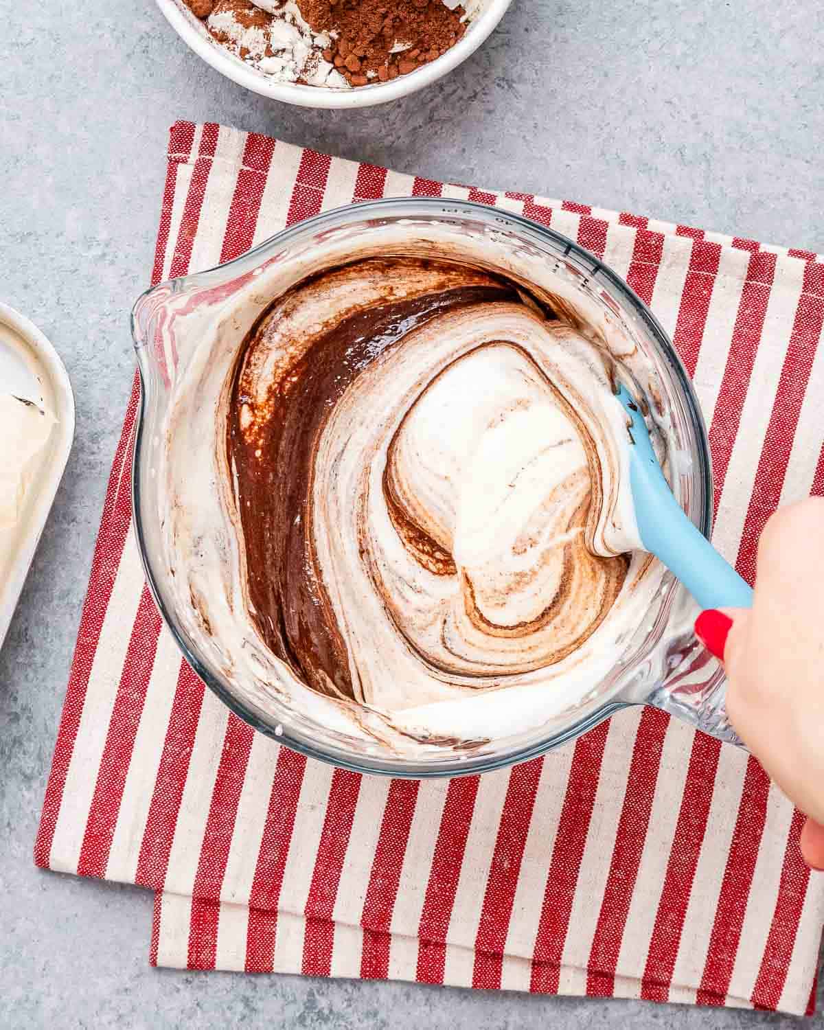 chocolate added over the milk and egg mixture and a blue spatula is mixing to combine.