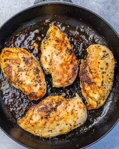 Searing chicken breast in a black pan.