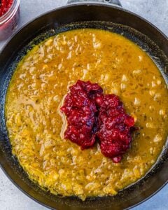 Adding cranberry sauce to an orange sauce in a pan.