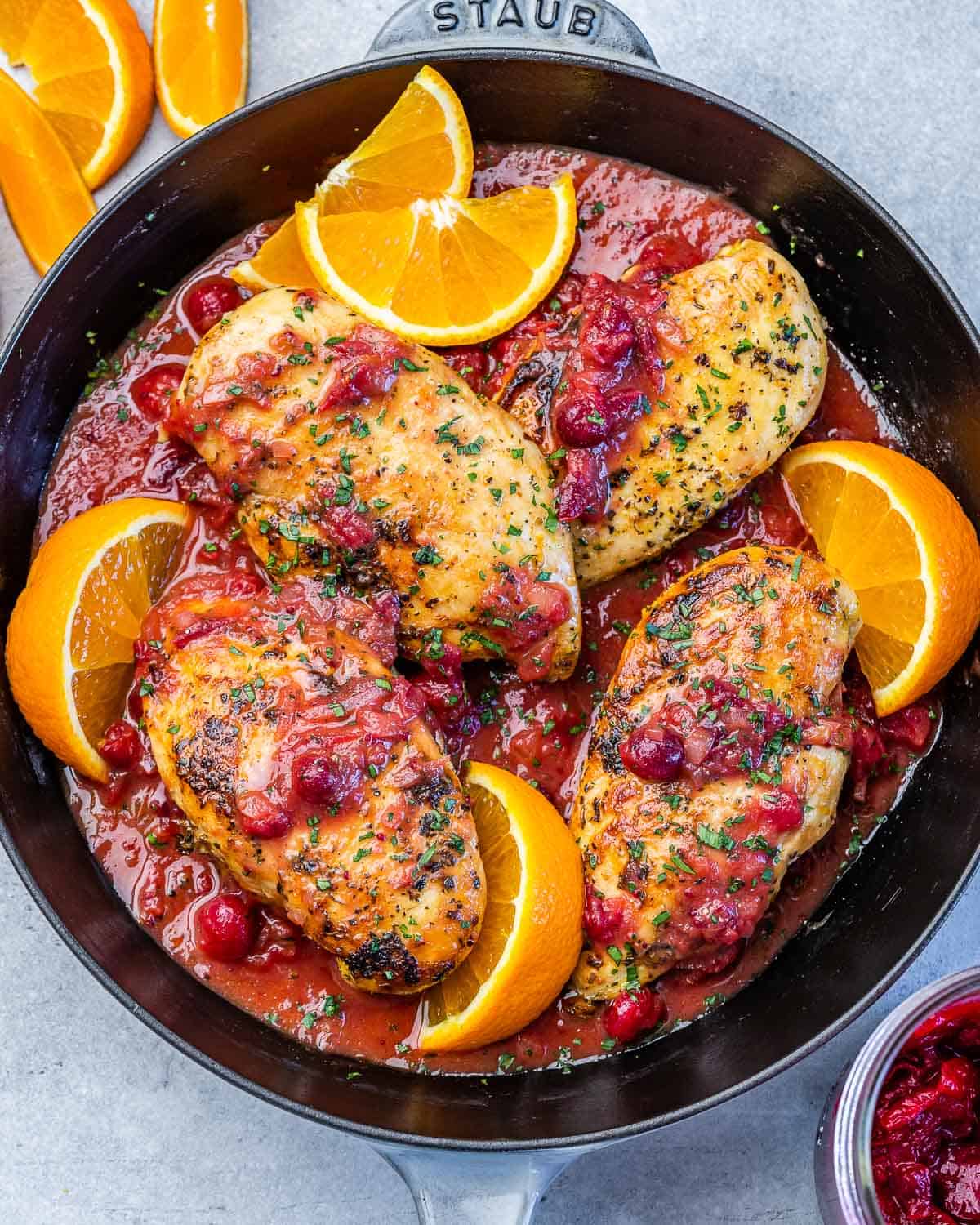 Top view of a black skillet that has 4 cooked chicken breasts in an orange cranberry sauce with orange slice garnishes around the chicken.