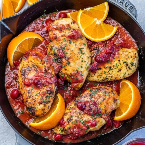 top view of a black skillet that has 4 cooked chicken breasts in an orange cranberry sauce with orange slice garnishes around the chicken