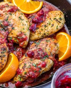 Chicken breasts cooked in a pan with cranberry sauce and oranges.