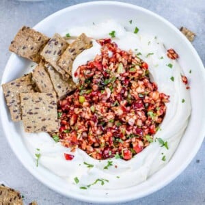 top view of a bowl of cream cheese topped with cranberry salsa with a side of crackers on the cheese next to the salad on the top left corner