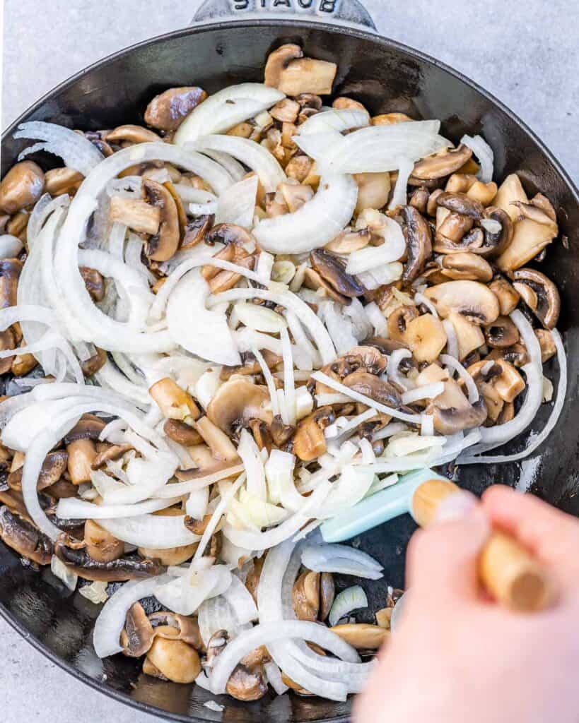 onions added over sauteed mushrooms in a black skillet