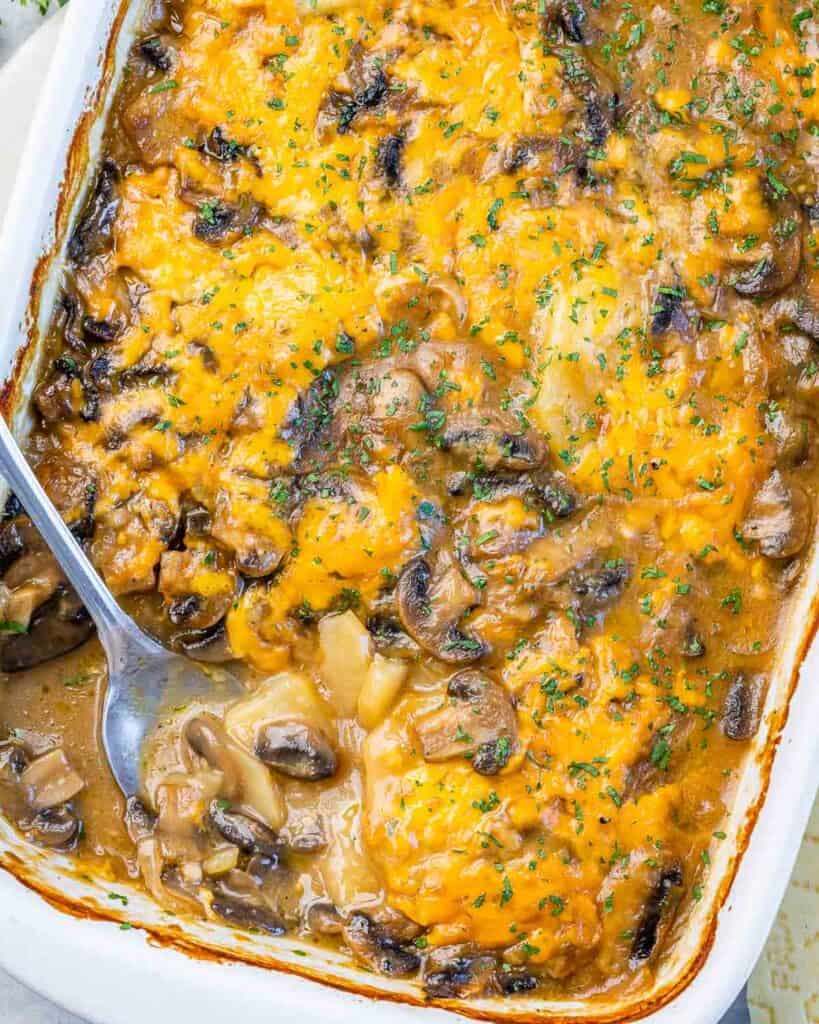 top close up view of baked cheesy potato and mushroom casserole with spoon on the lower left side of the dish