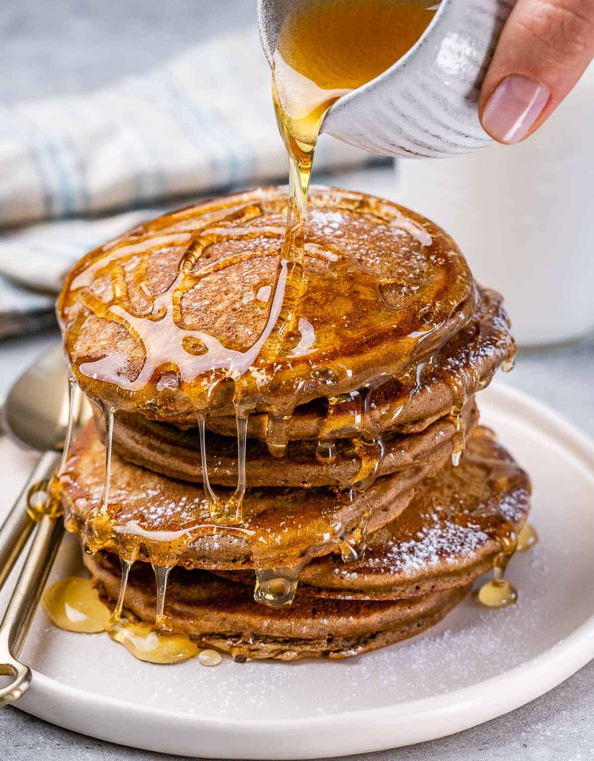 Drizzling honey over a stack of gingerbread pancakes on a white plate.