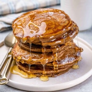 side shot of stacks of pancakes on a white plate with honey drizzled over