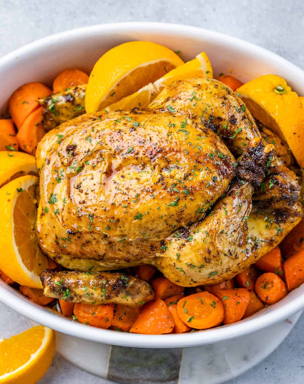 A white baking dish with baked chicken over chopped carrots and orange slices.