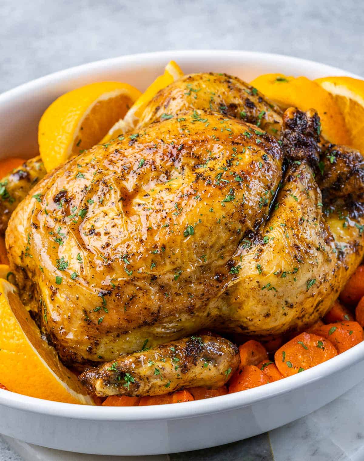 a baked whole chicken in a dish with carrots at the bottom of the dish.