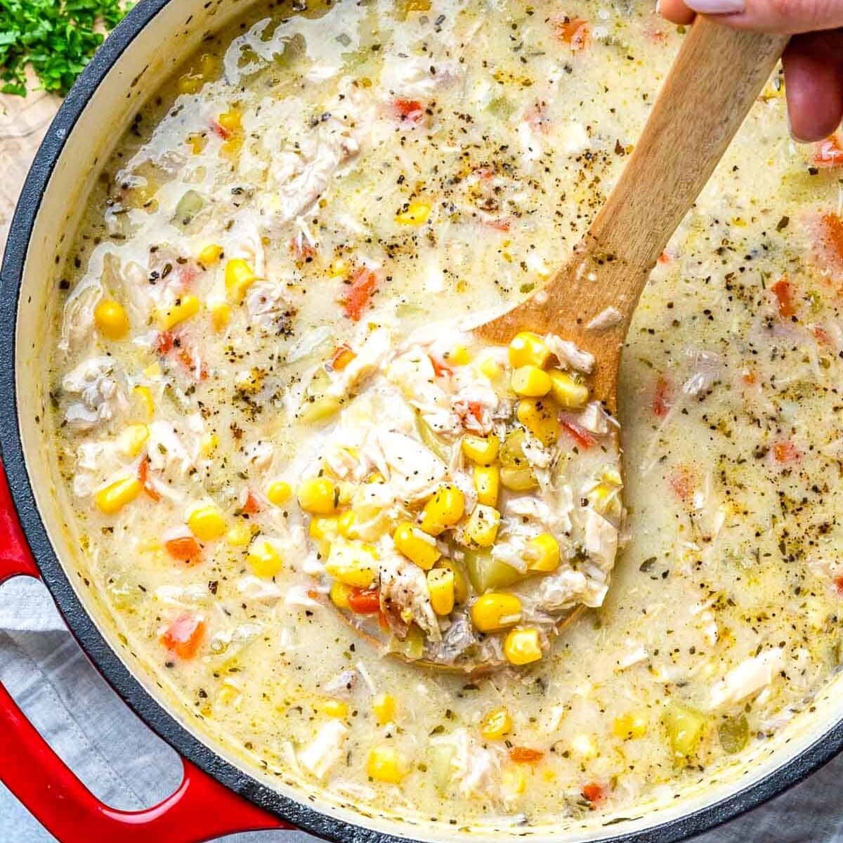 grabbing a spoonful of corn chowder soup from the filled soup pot.