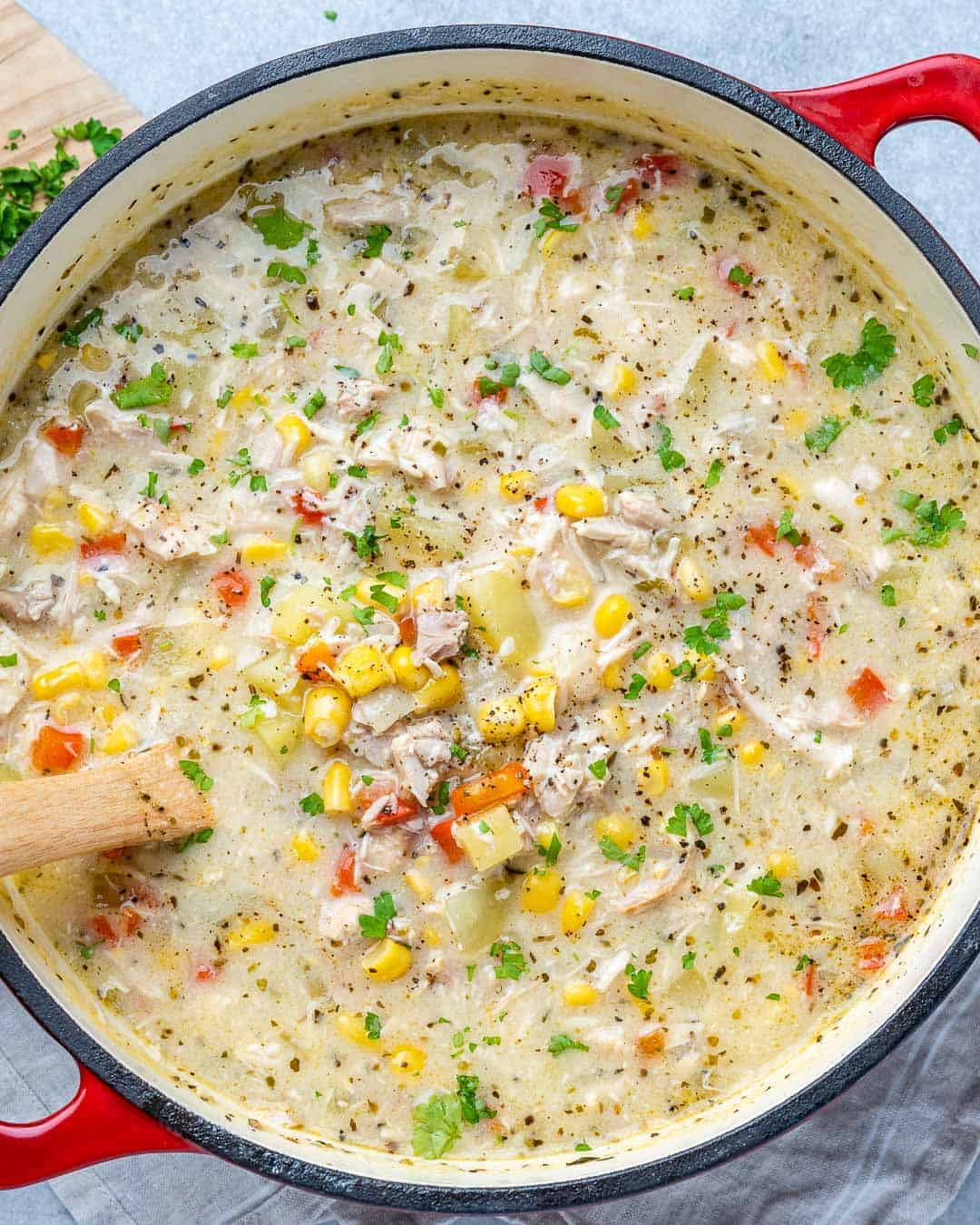 Red pot of chicken Corn Chowder with a wooden spoon inside.