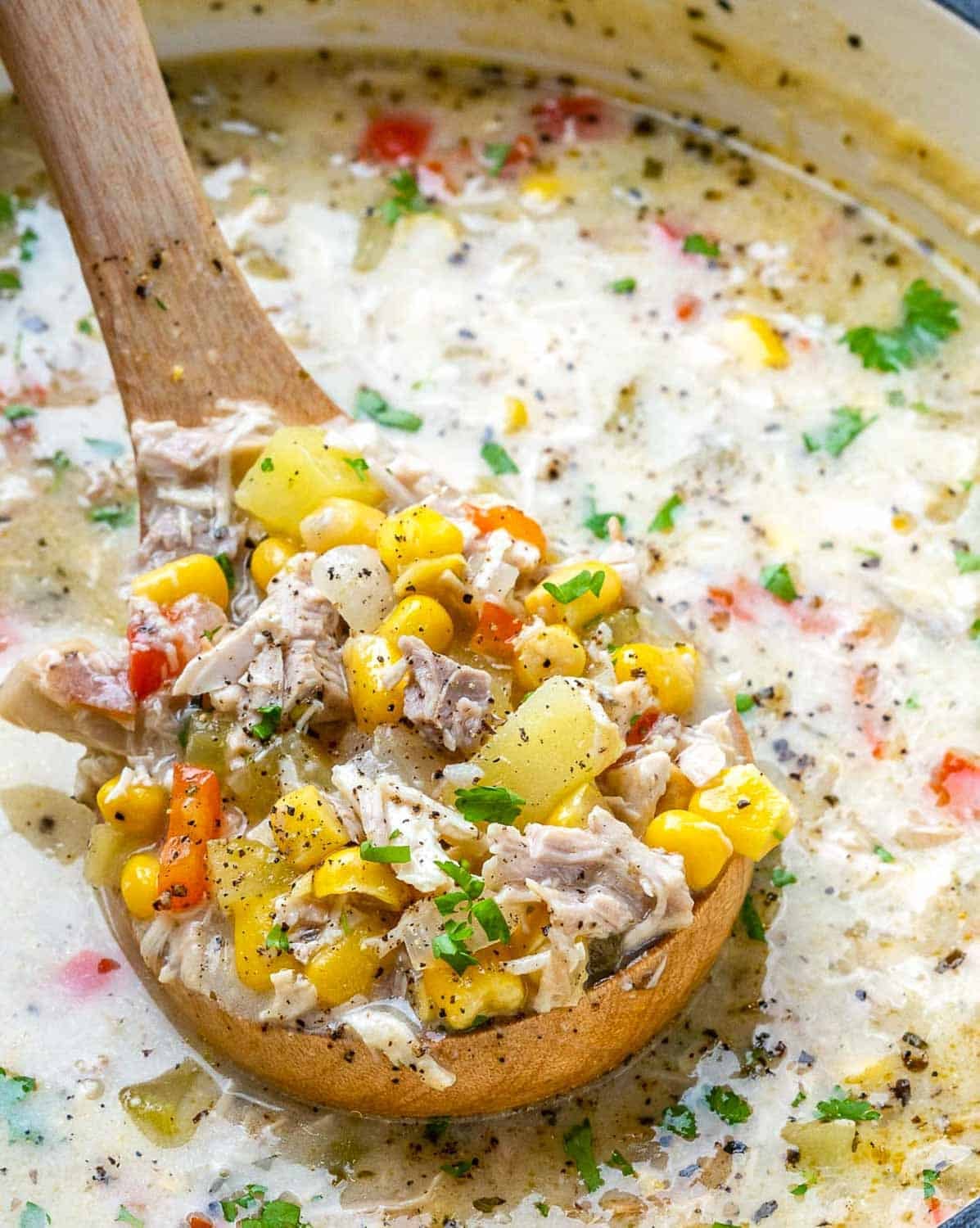 a pot with chicken corn chowder and a spoon full coming out of the pot.